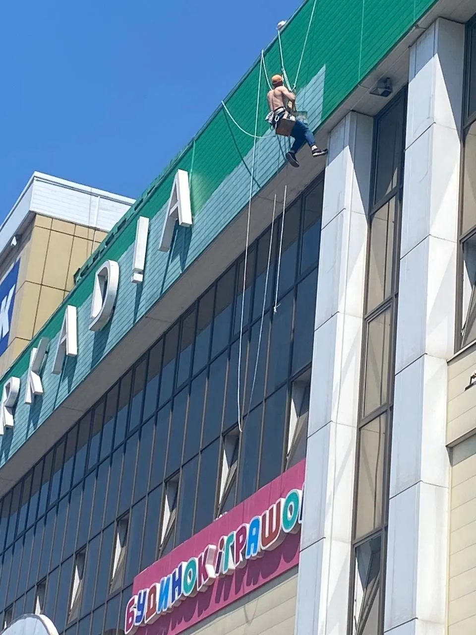 Промисловий альпініст фарбує фасад торгового центру на висоті